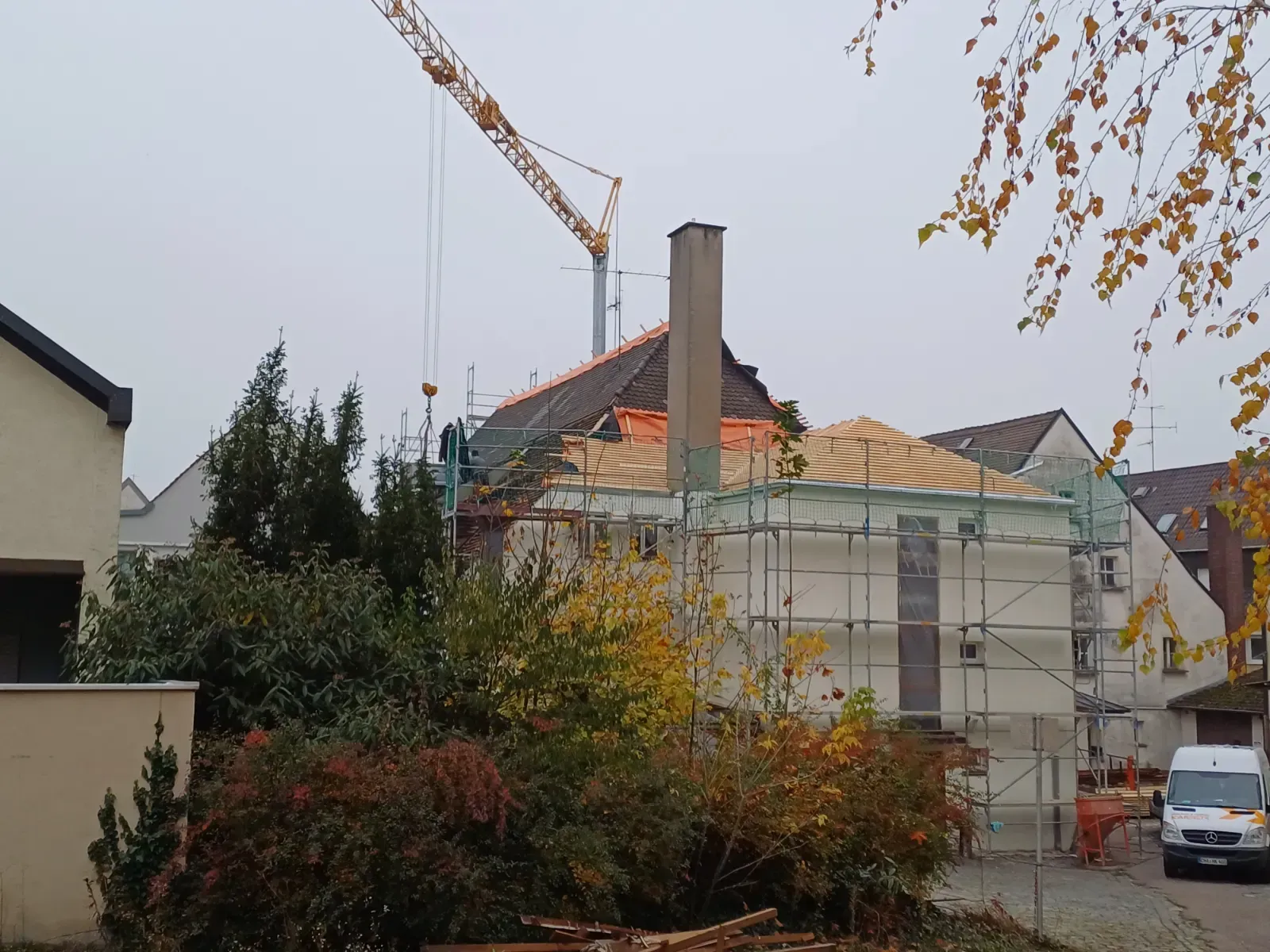 Haus im Bau mit Gerüst und Kran hinter einer Hecke an einem bewölkten Tag