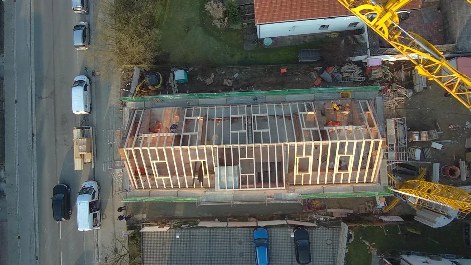 Luftaufnahme eines im Bau befindlichen Gebäudes neben einer Straße mit geparkten Autos und Kränen.