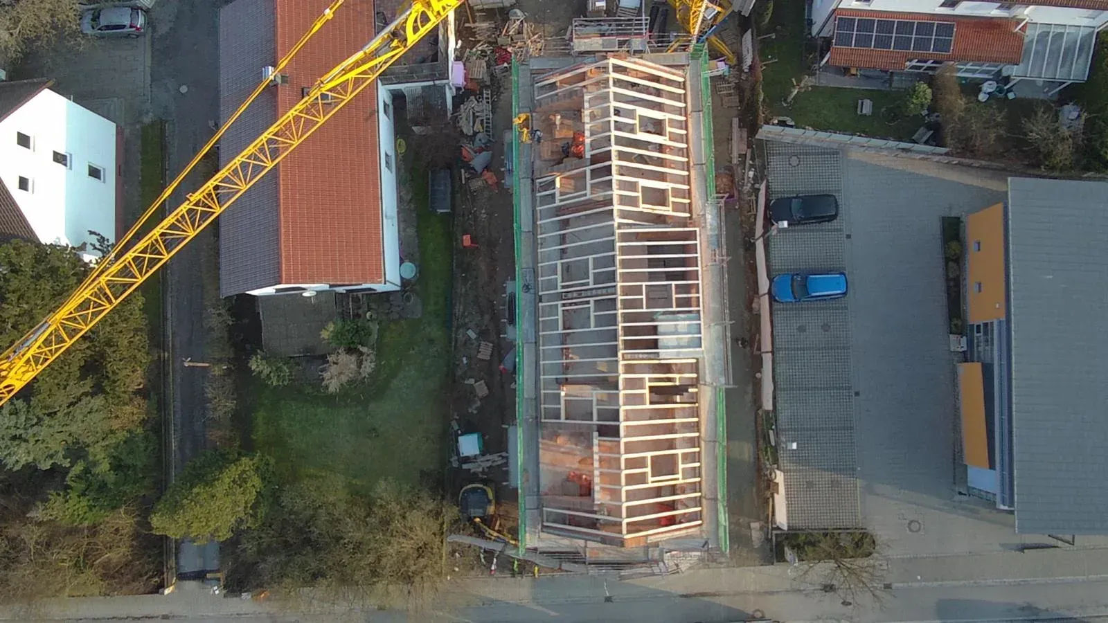 Luftaufnahme einer Baustelle mit Kran, unfertigem Dachstuhl und umliegenden Gebäuden.