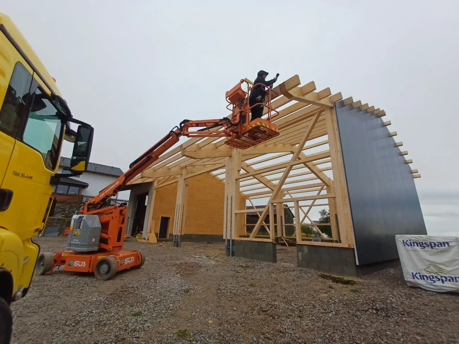 Arbeiter errichten mit einem Kran und einer Hebebühne ein Holzdach auf einer Baustelle.