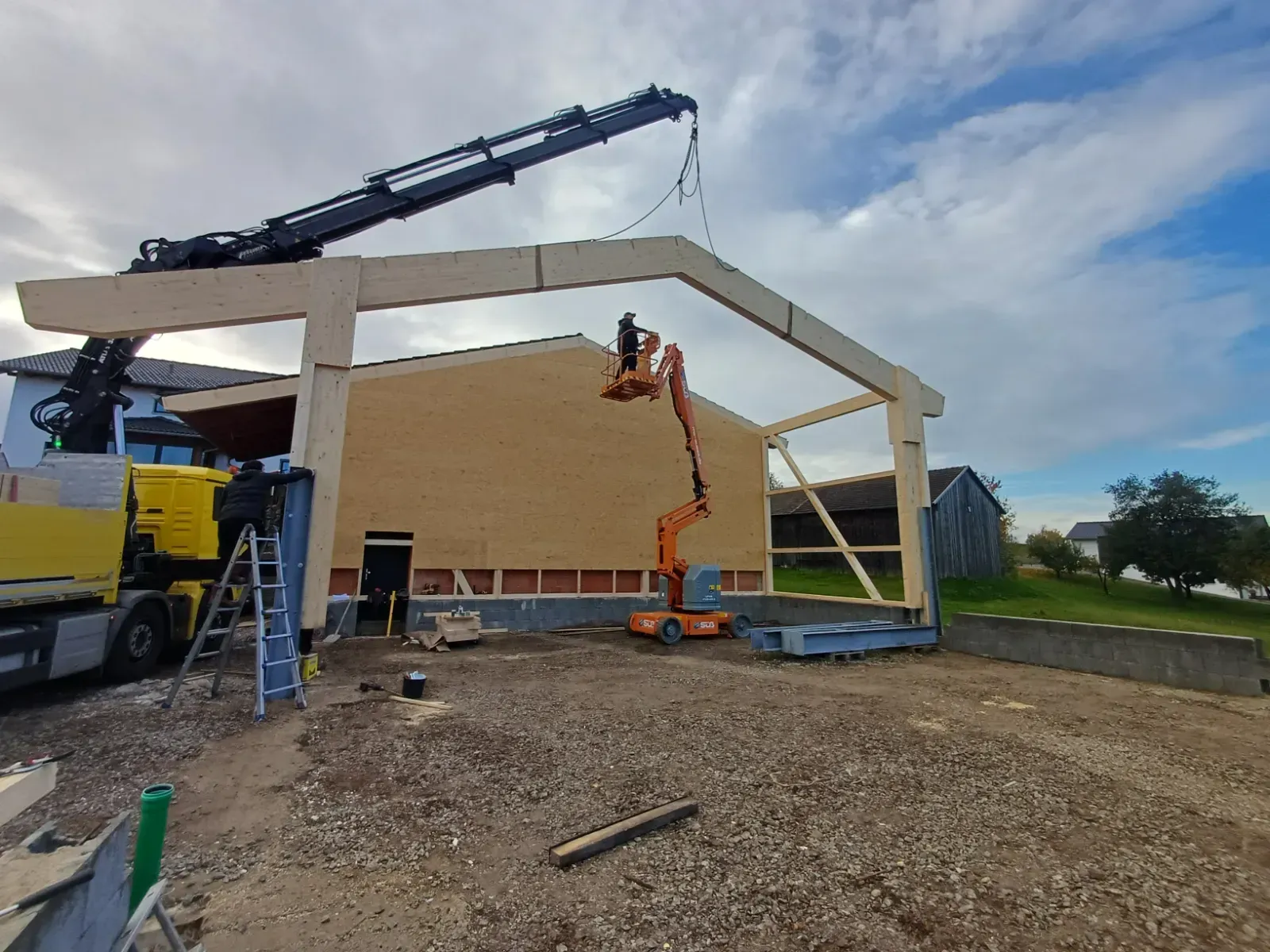 Baustelle mit Kran, der ein Stahlgerüst über ein im Bau befindliches Gebäude hebt.
