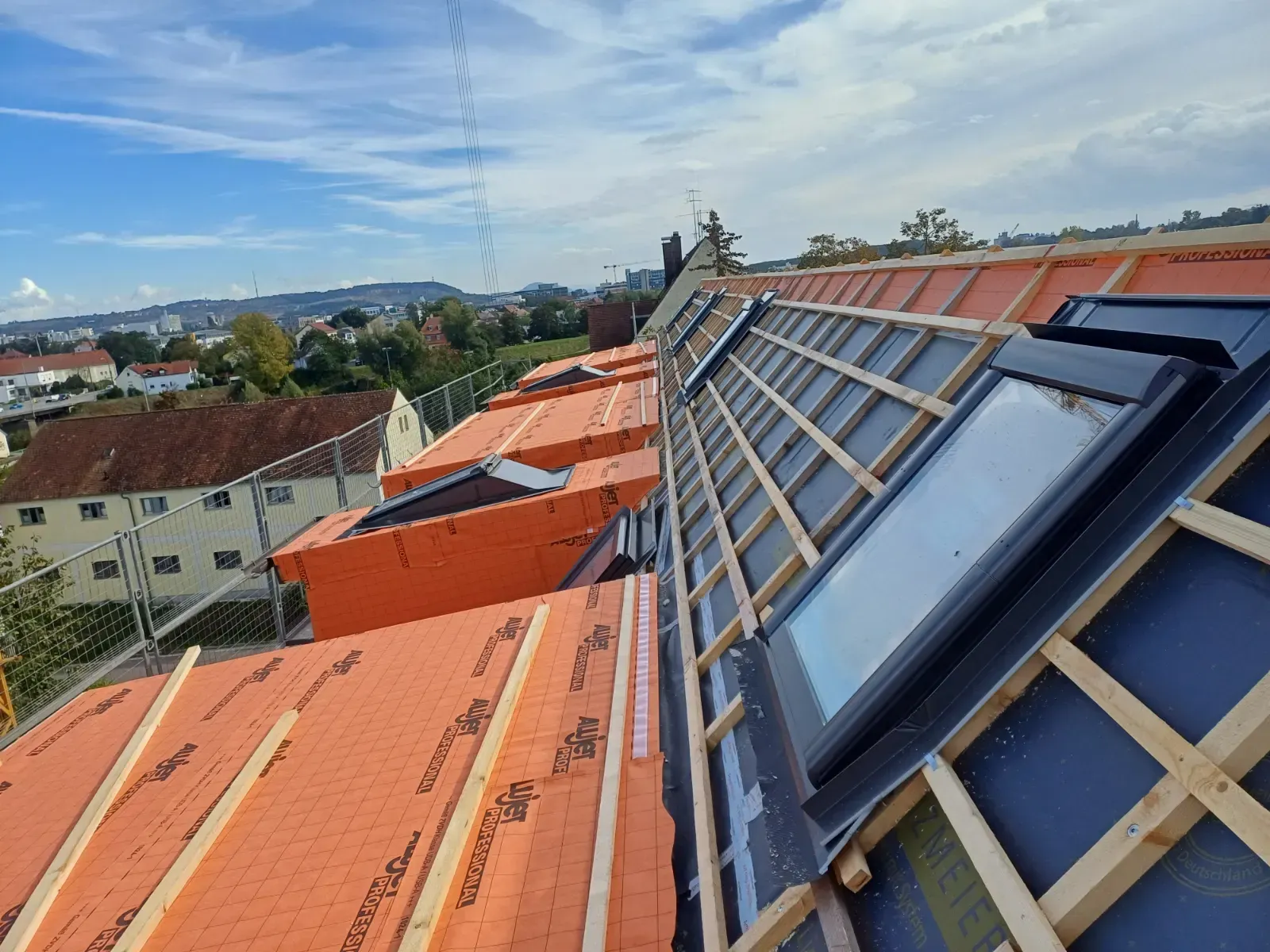 Ein Dach im Bau mit orangefarbenen Ziegeln und blauen Oberlichtpaneelen an einem sonnigen Tag