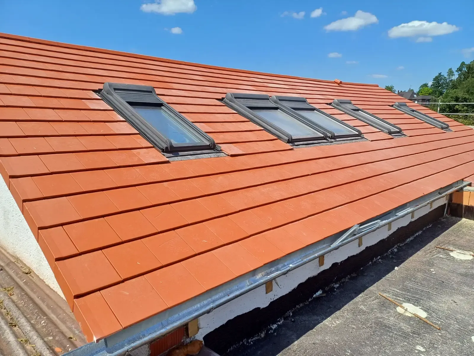 Ein Haus mit orangefarbenem Ziegeldach und mehreren Dachfenstern unter blauem Himmel