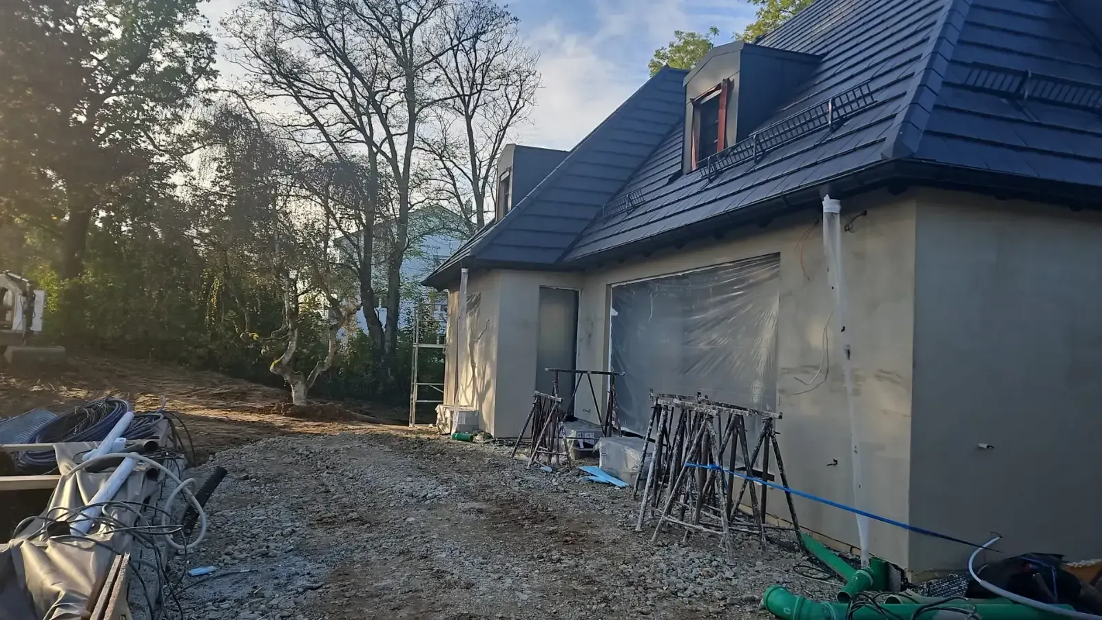 Teilweise renoviertes Haus mit dunklem Dach, unfertigen grauen Wänden und Baumaterialien an der Außenseite