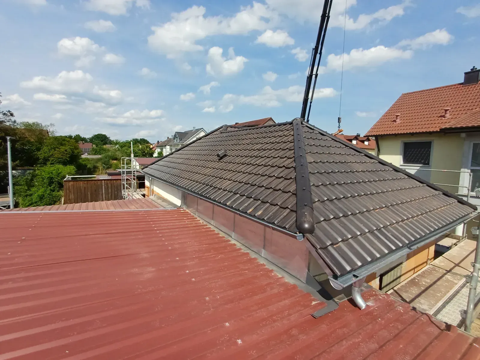 Ein Dach mit grauen Schindeln und ein rotes Flachdach unter blauem Himmel mit Wolken.