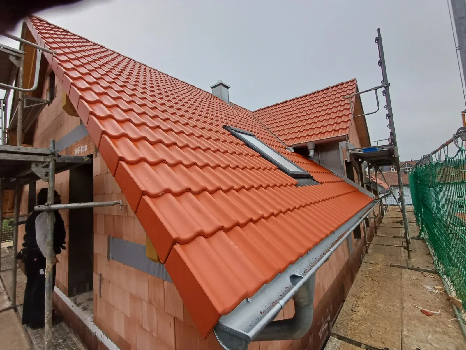 Ein im Bau befindliches, rotziegeliges Dach auf einem Backsteinhaus, daneben ein Gerüst und eine Leiter.