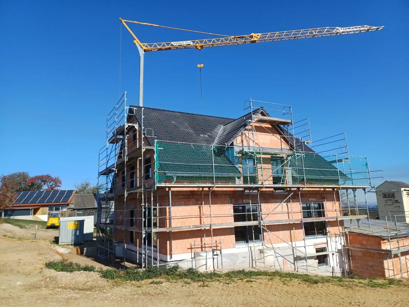 Haus im Bau mit Gerüst und Kran vor klarem, blauem Himmel