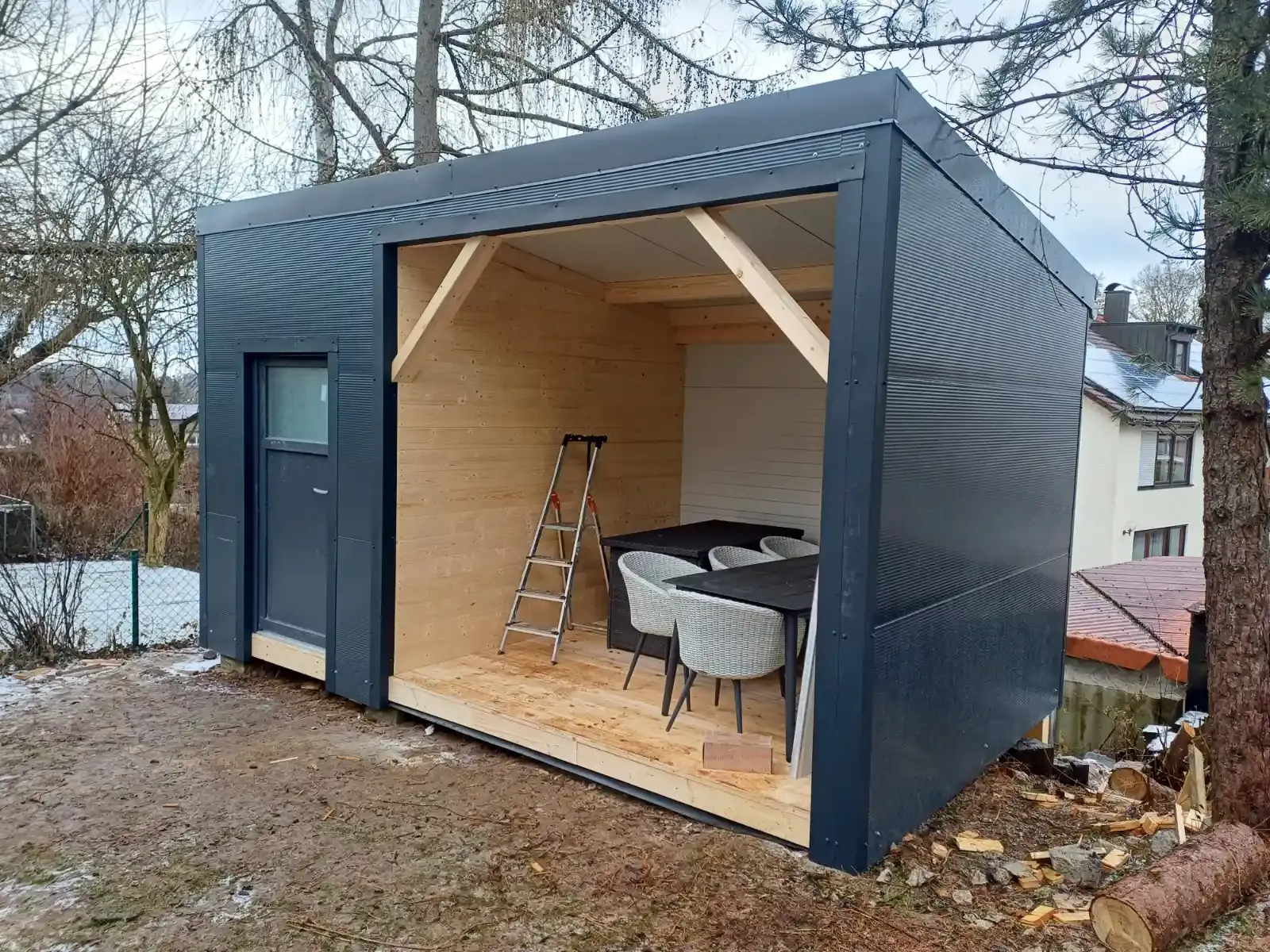 Kleiner, moderner Gartenschuppen aus Holz mit offener Vorderseite, Leiter und Gartenmöbeln im Inneren