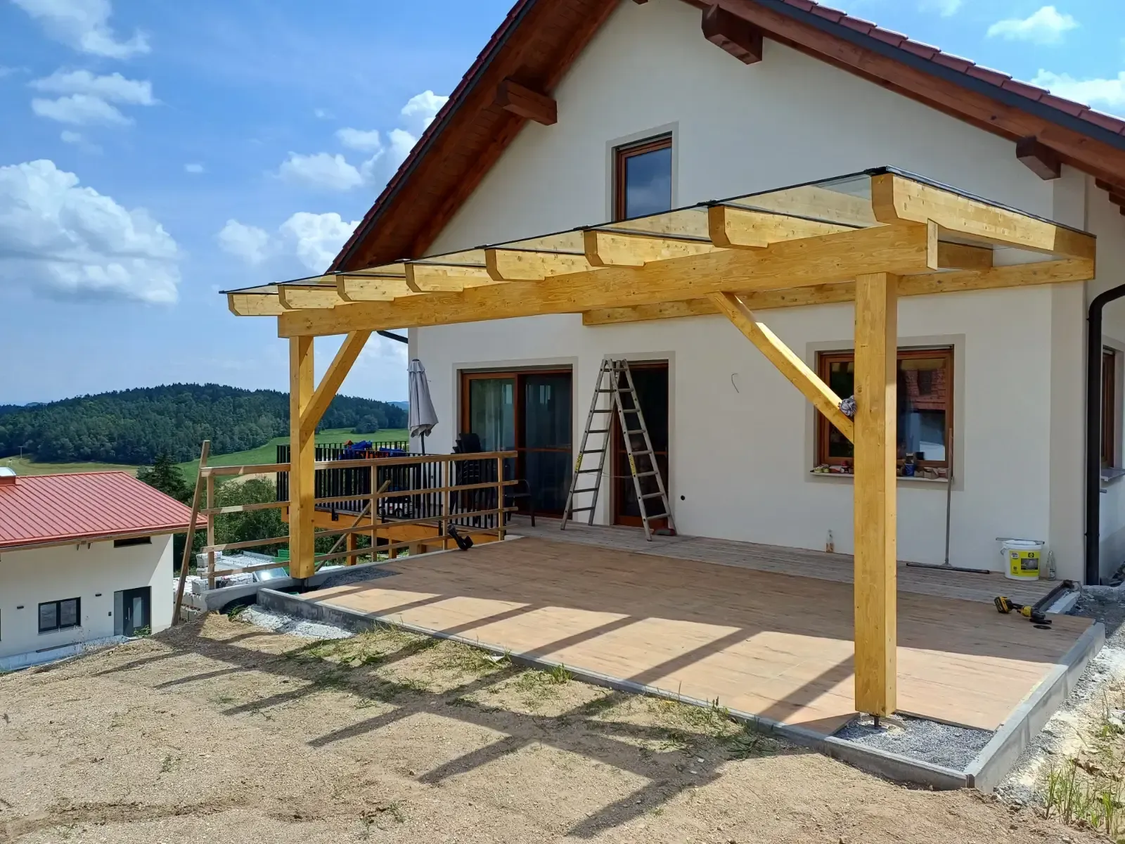 Terrasse mit im Bau befindlicher Holzpergola neben einem weißen Haus und blauem Himmel