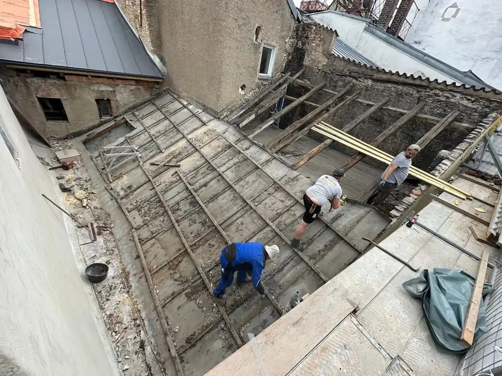Arbeiter reparieren ein beschädigtes Dach mit freiliegenden Balken und Planen an einem Steingebäude.