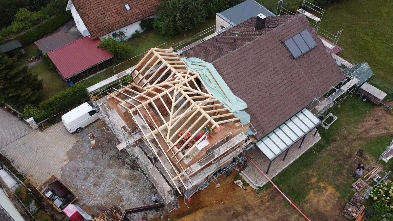 Luftaufnahme eines Hauses mit im Bau befindlichem Dach, freiliegende Holzkonstruktion und Dachmaterialien sind sichtbar.