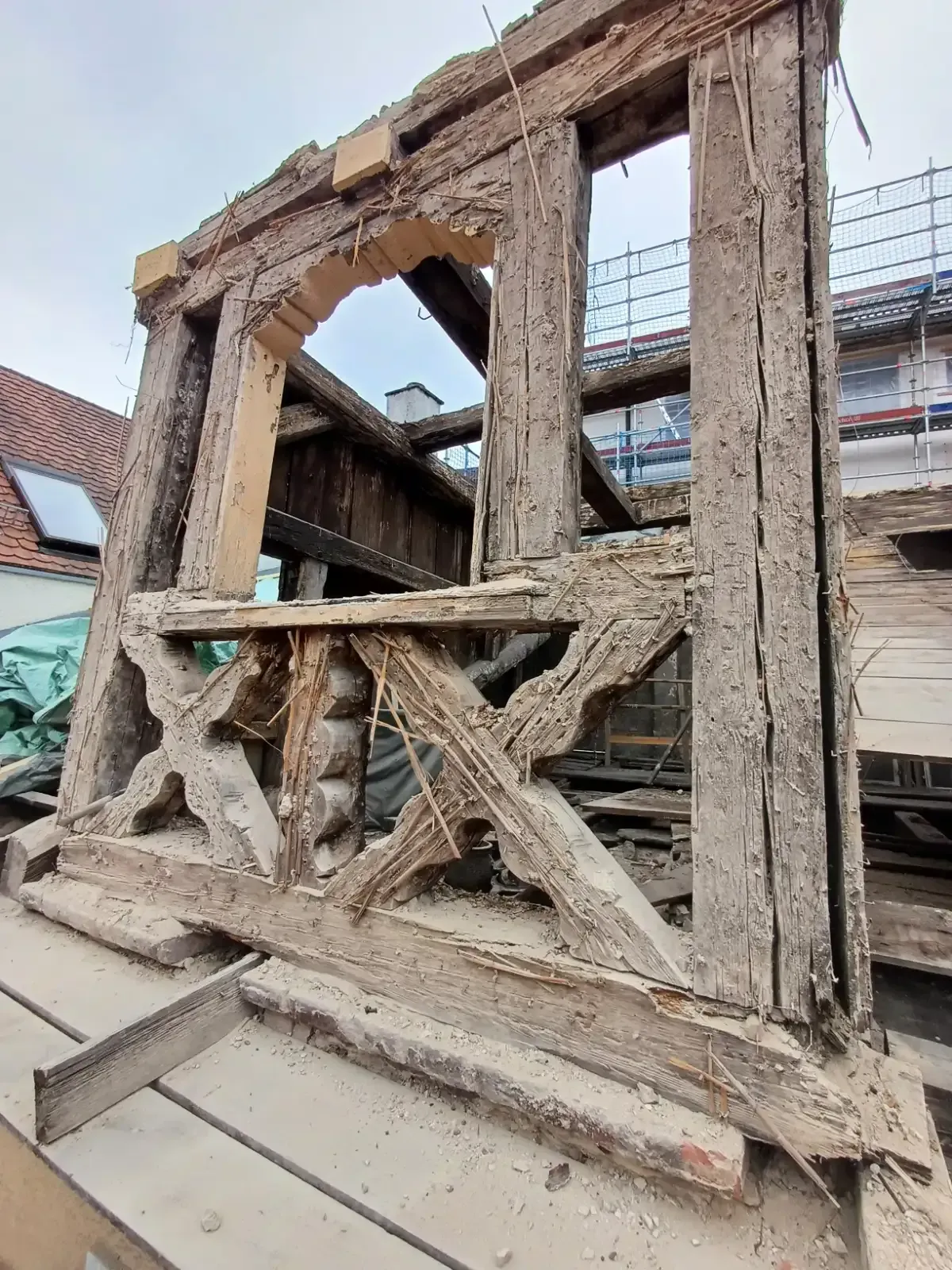 Beschädigte Holzfassade eines Gebäudes mit gebrochenen Balken und freiliegendem Innenraum, von einer Straße aus gesehen.