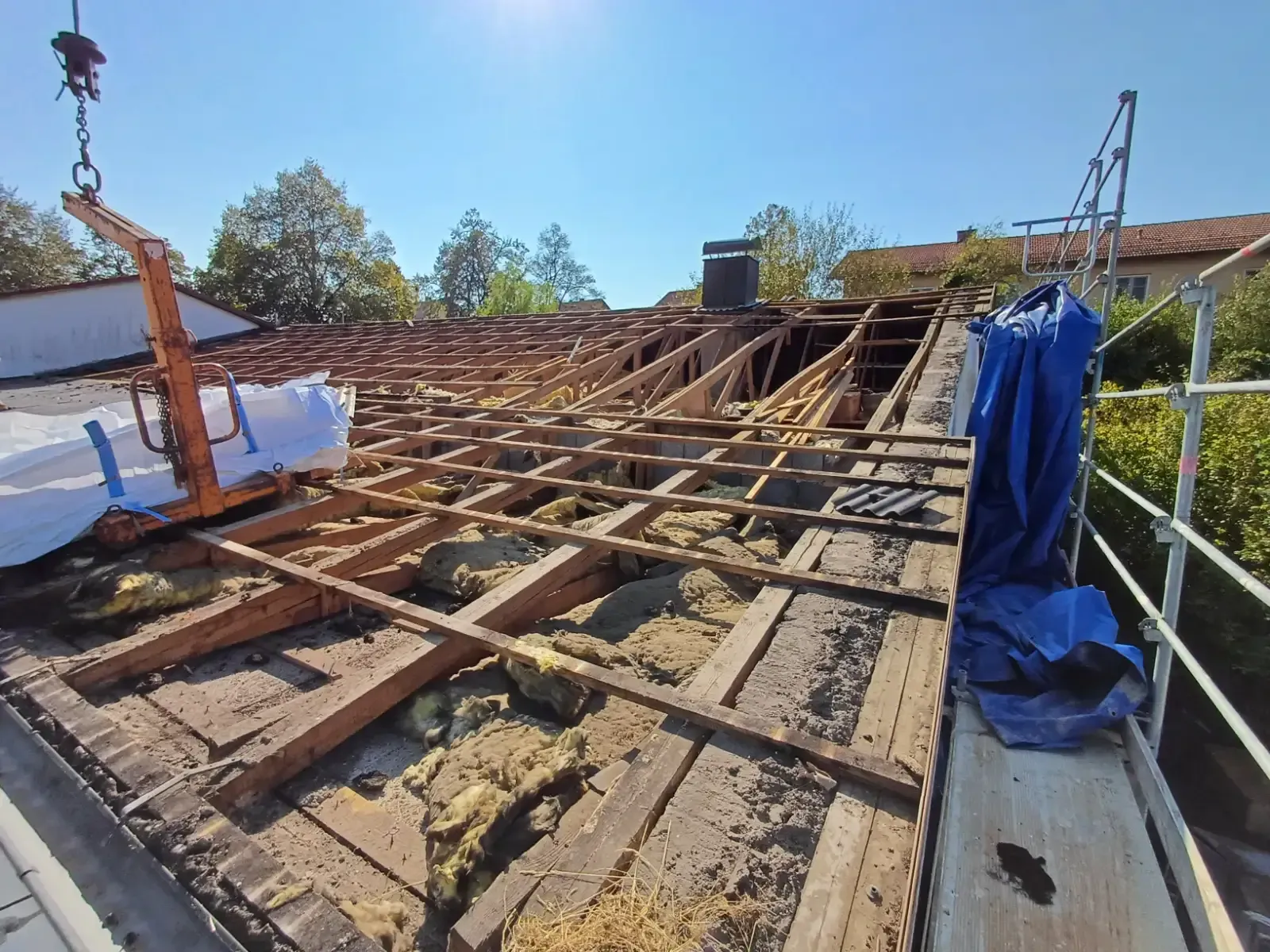 Dach im Bau mit freiliegenden Holzbalken, Gerüst und blauer Plane im hellen Tageslicht
