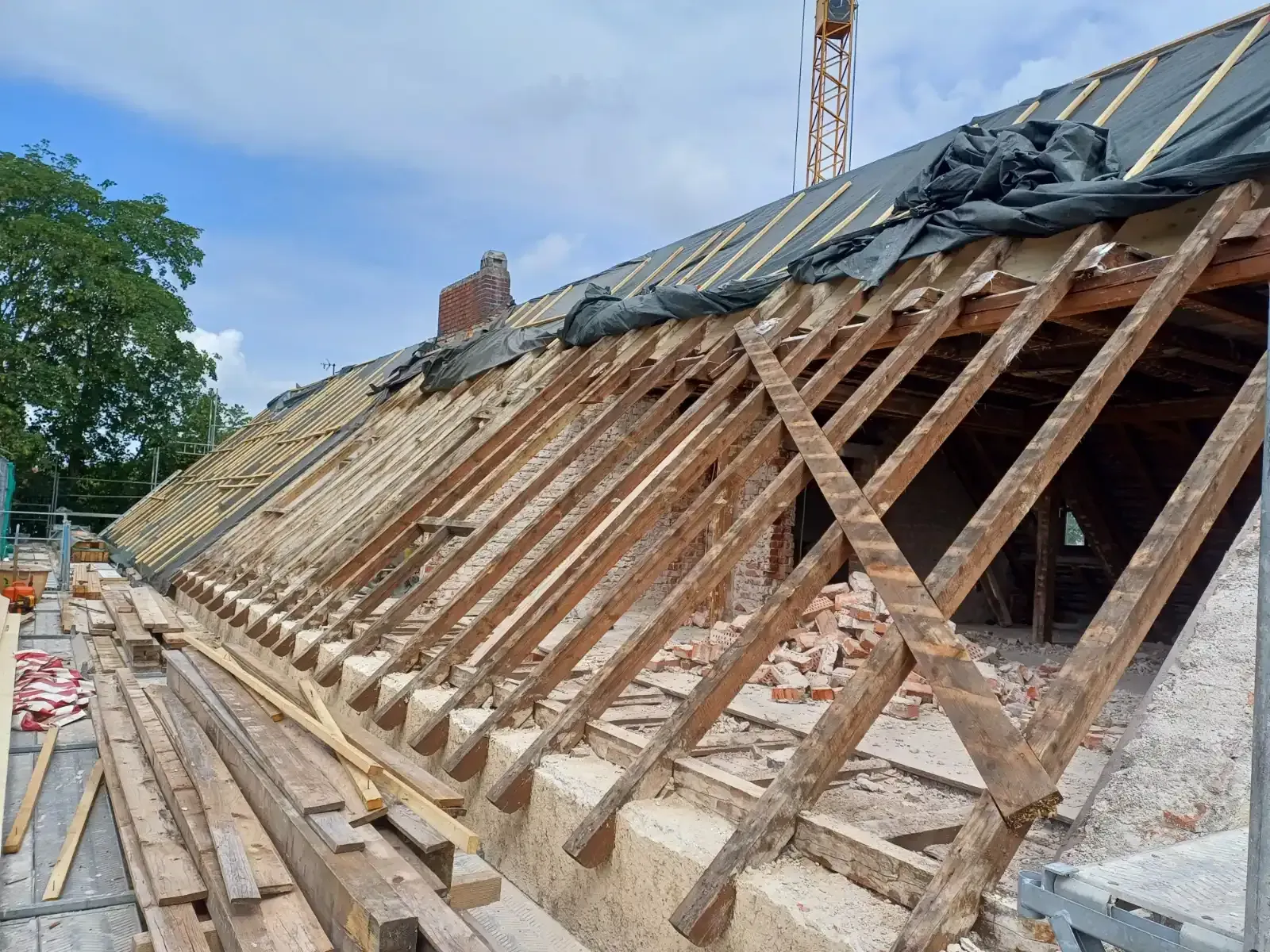 Das Dach wird repariert; an der Gebäudeaußenseite sind die Holzsparren freigelegt, Bauschutt und ein Gerüst zu sehen.