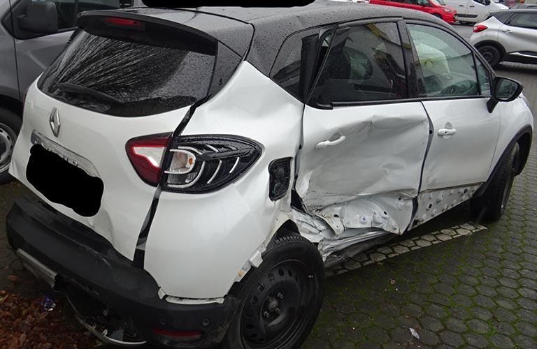 Auf einem Parkplatz steht ein weißes Auto mit beschädigtem Heck.
