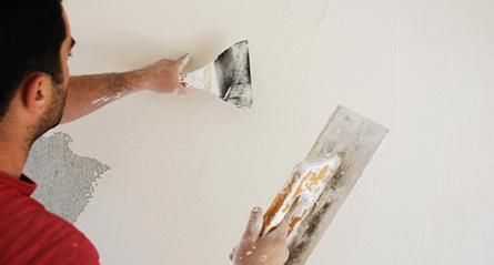 Persona aplicando yeso a una pared con una paleta, cubriendo un agujero.