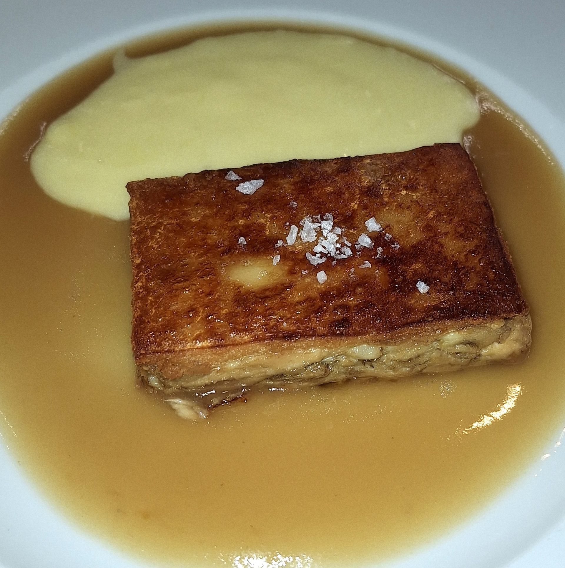 Una rebanada rectangular de pan o pastel, dorada a la sartén y cubierta con sal gruesa, servida en una salsa marrón con puré.