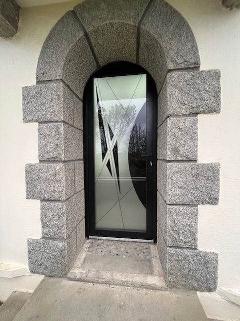 Porte cintrée en pierre avec porte en verre foncé et motif en X diagonal dépoli