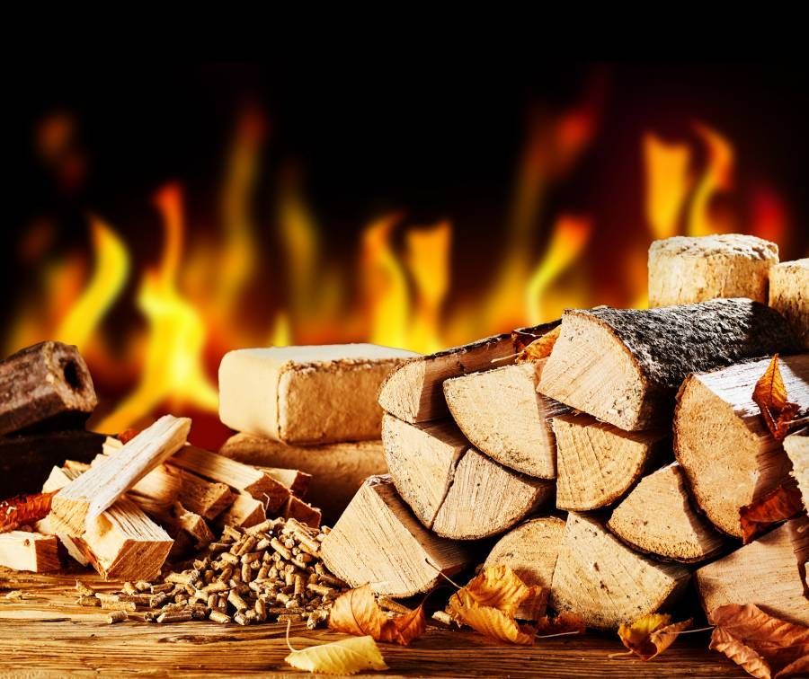 Gestapelte getrocknete Holzscheite vor einem brennenden Feuer in einer kalten Herbstnacht mit Holzpellets und Ziegeln
