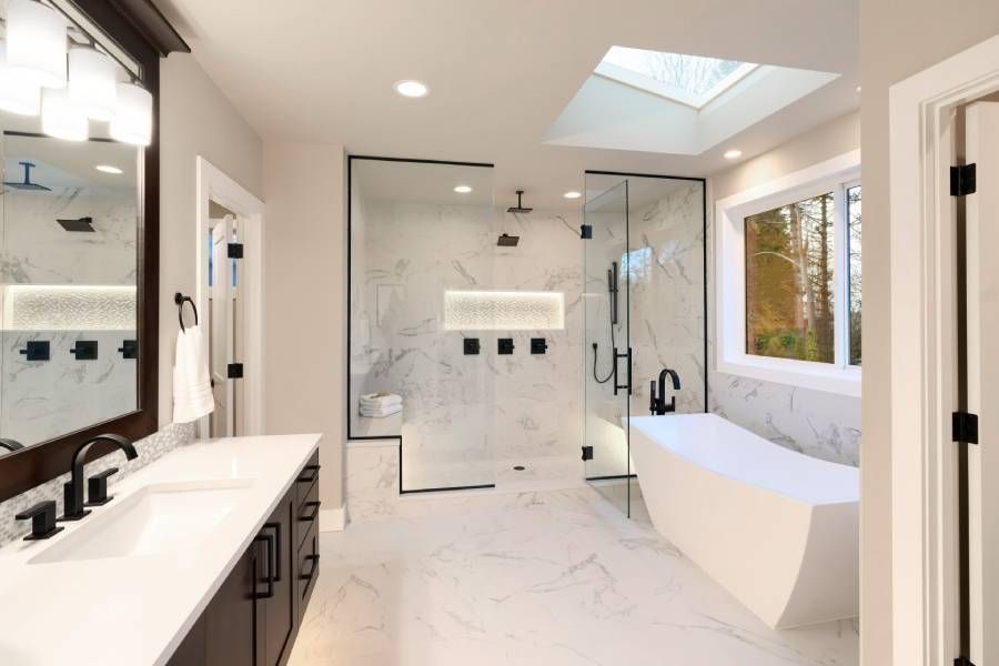 Luxuriöses, modernes Badezimmer mit dunkelbraunen Schränken, weißem Marmor, begehbarer Dusche, freistehender Badewanne, zwei Spiegeln und Blumen.
