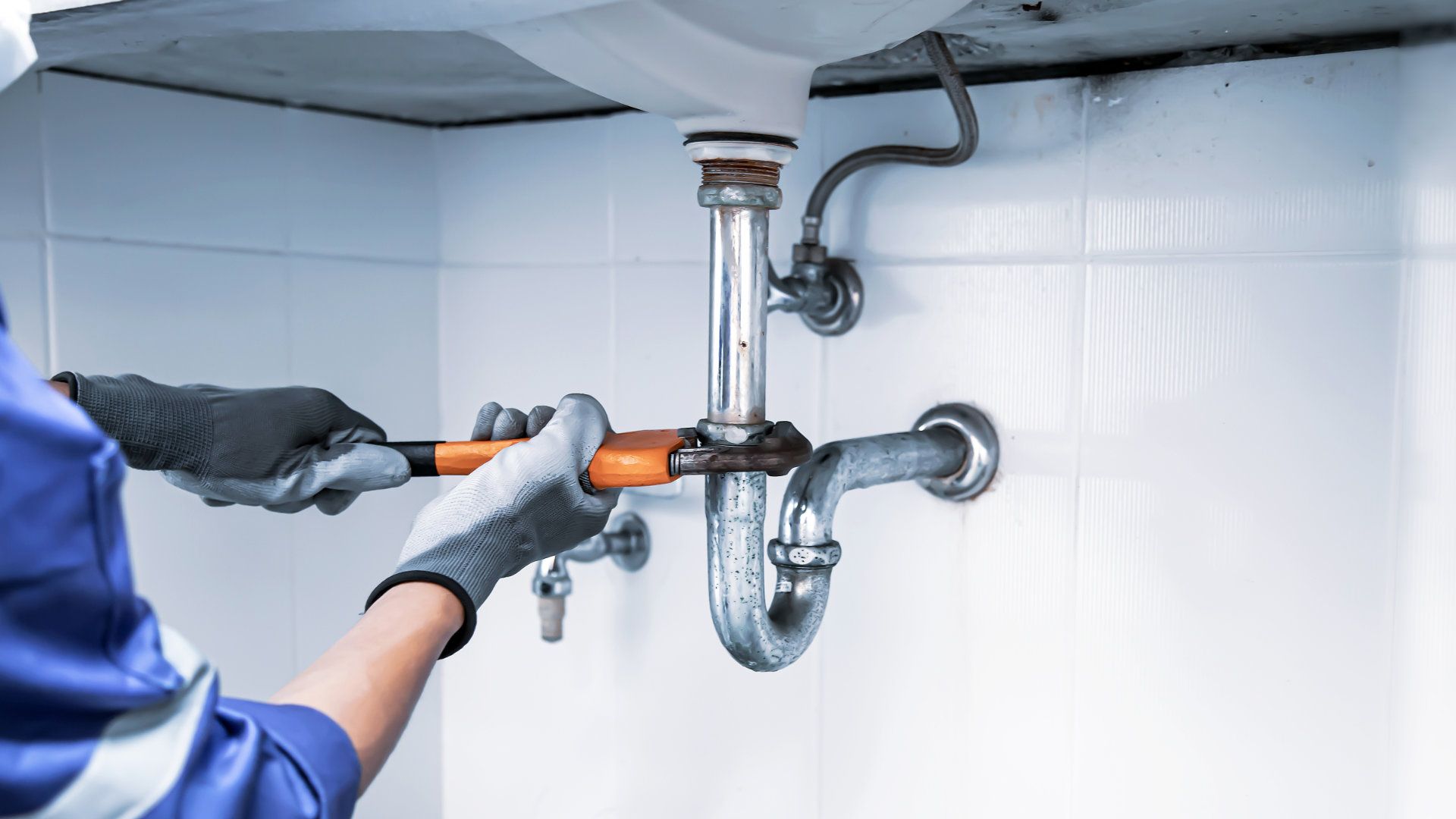 Techniker Klempner mit einem Schlüssel zur Reparatur einer Wasserleitung unter dem Waschbecken. Konzept der Wartung, fixieren Wasser-Klempner Lecks, ersetzen Sie die Küchenwanne Abfluss, Reinigung verstopften Rohre ist schmutzig oder rostig.