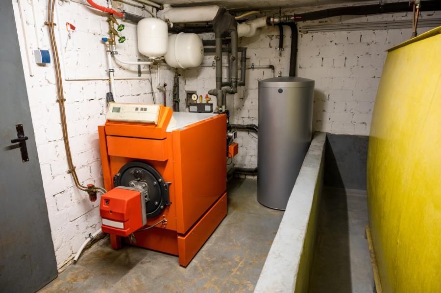 Alte Ölheizung mit Öltank und Warmwasserspeicher im Keller eines Einfamilienhauses - Heizen mit fossilen Brennstoffen