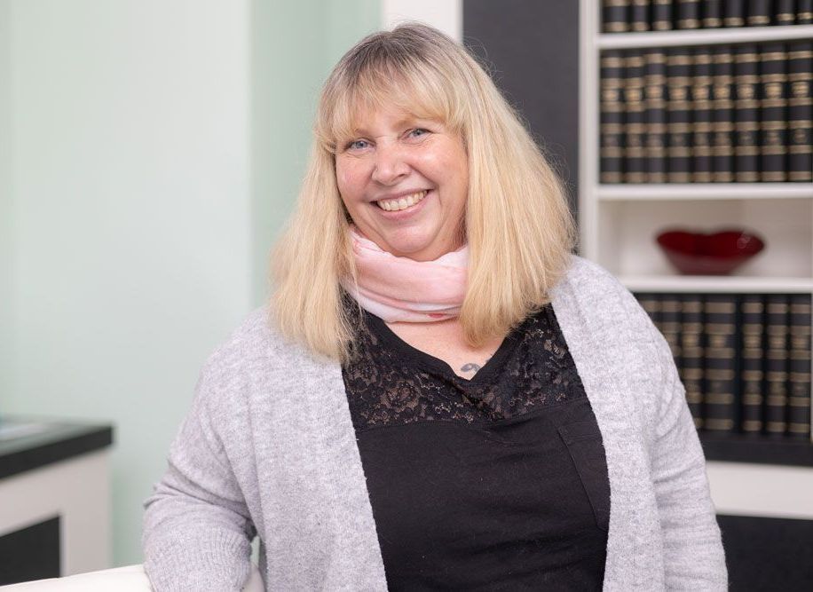 Eine Frau lächelt vor einem Bücherregal.