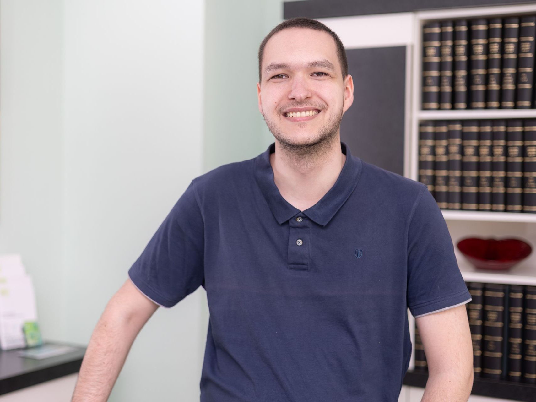 Ein Mann in einem blauen Hemd steht vor einem Bücherregal.