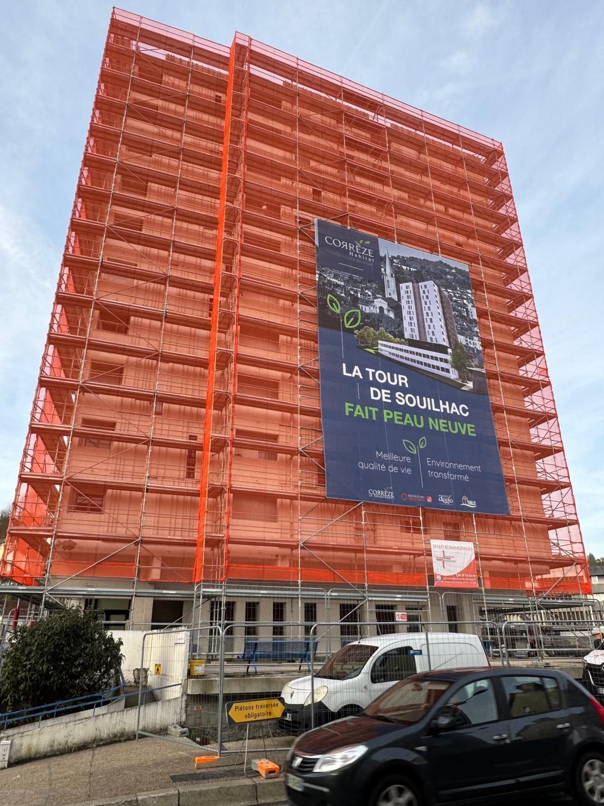 Échafaudage et filet antigravats installés autour d'un grand immeuble - affiche des travaux affichée dessus