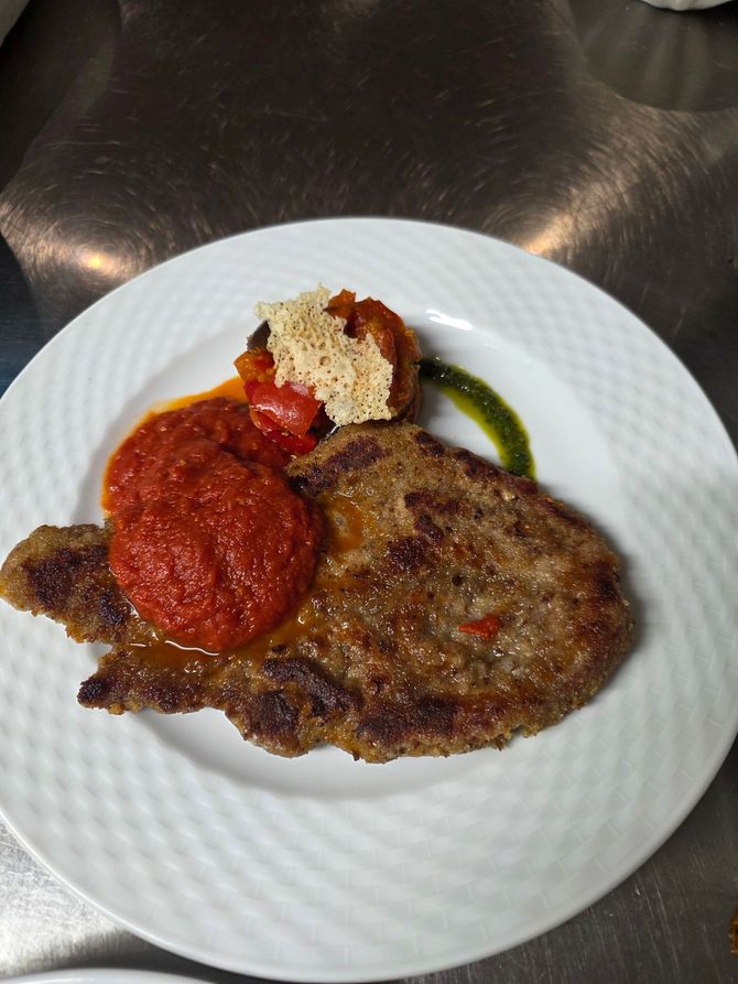 Assiette de viande grillée nappée de sauce rouge, accompagnée d’une garniture et d’un filet de sauce verte, sur une assiette blanche.