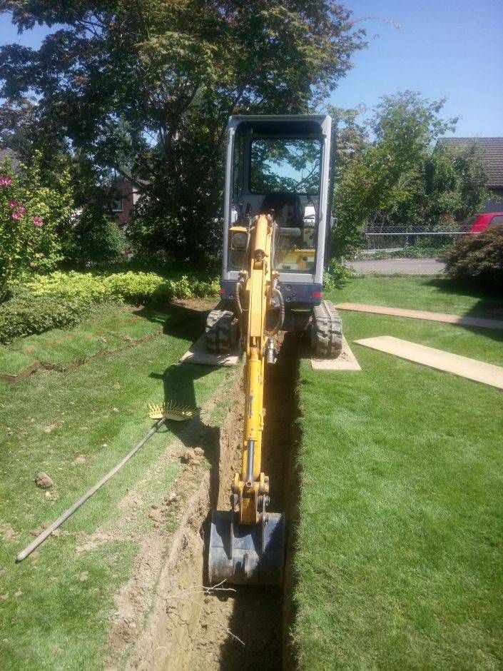 Ein kleiner gelber Bagger gräbt in einem Hof ​​einen Graben. Foto von der Sonderegger Gartenbau GmbH
