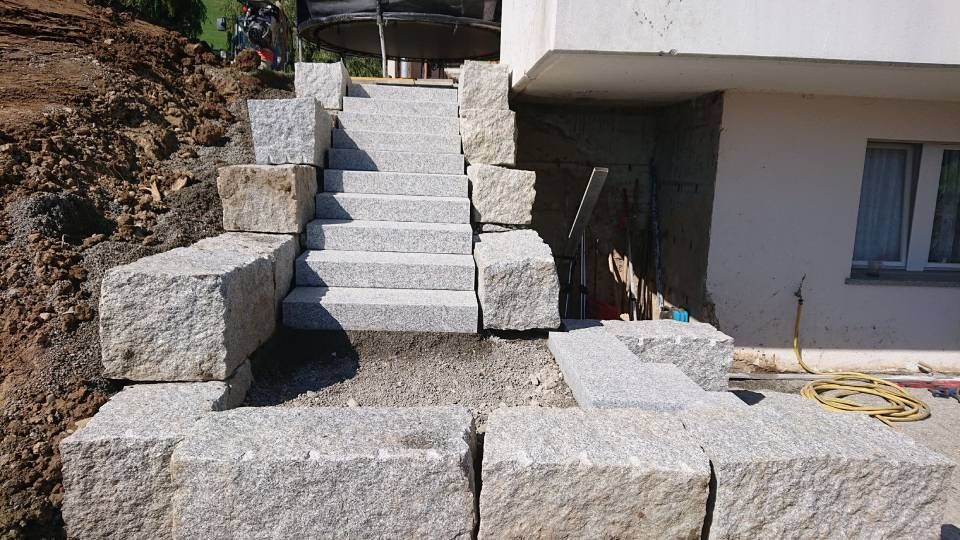 Eine Treppe aus Granitblöcken vor einem Gebäude. Foto von der Sonderegger Gartenbau GmbH