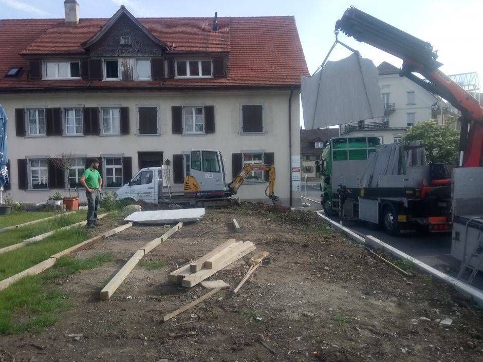Ein Kran hebt ein Stück Holz vor einem Gebäude an. Foto von der Sonderegger Gartenbau GmbH