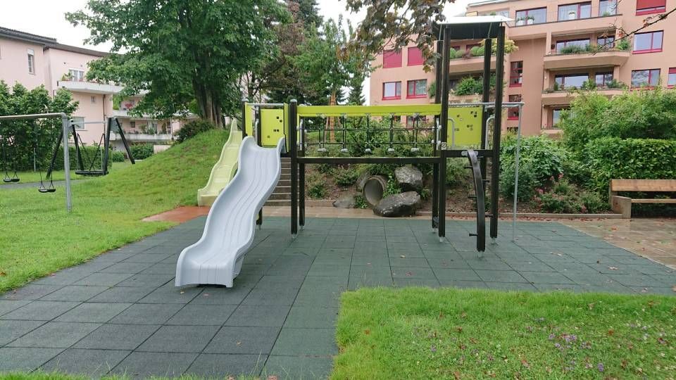Ein Spielplatz mit Rutsche und Schaukeln in einem Park. Foto von der Sonderegger Gartenbau GmbH