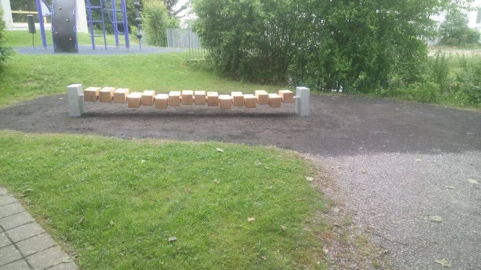Eine Holzbank in einem Park mit einem Spielplatz im Hintergrund. Foto von der Sonderegger Gartenbau GmbH