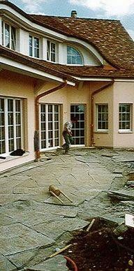 Ein Mann arbeitet auf einer Terrasse vor einem grossen Haus. Foto von der Sonderegger Gartenbau GmbH