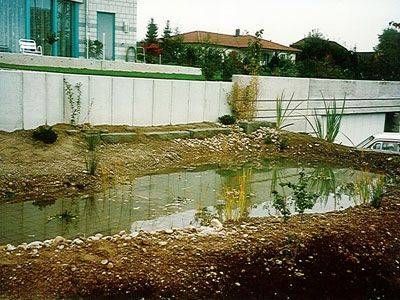 Vor einem Haus ist ein kleiner Teich, umgeben von Erde und Steinen.