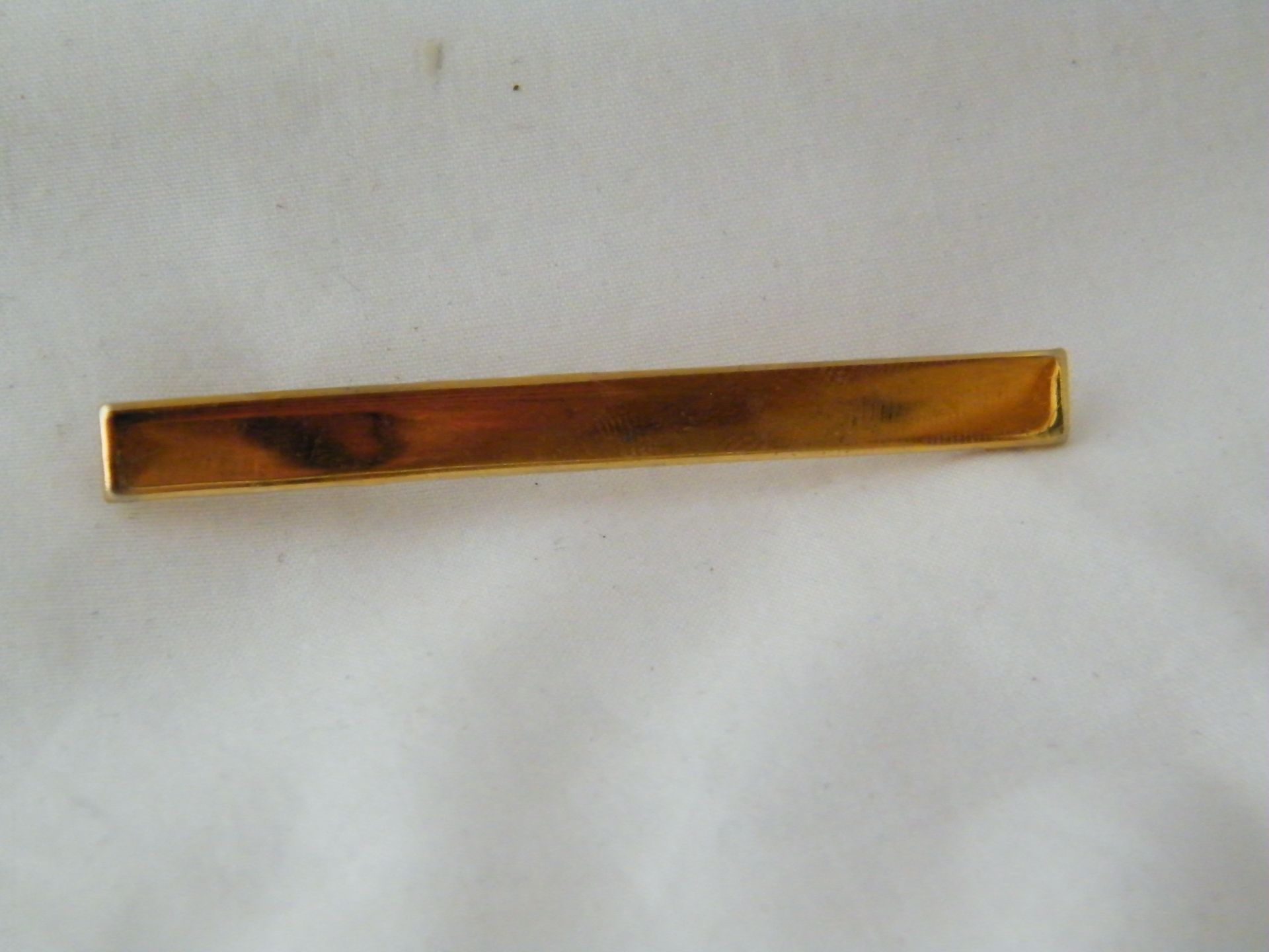 Una barra de corbata de oro reposa sobre una superficie blanca