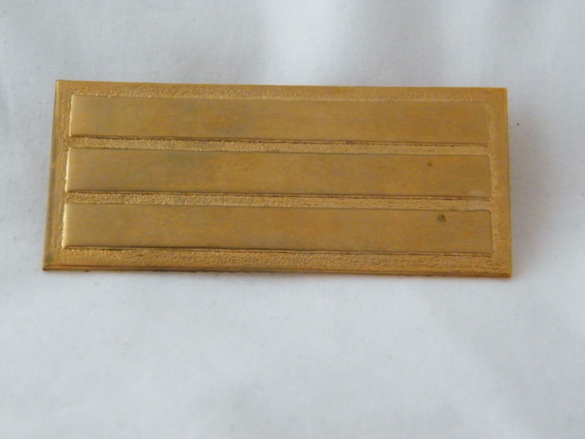 Una placa de oro con tres líneas está sobre una superficie blanca.