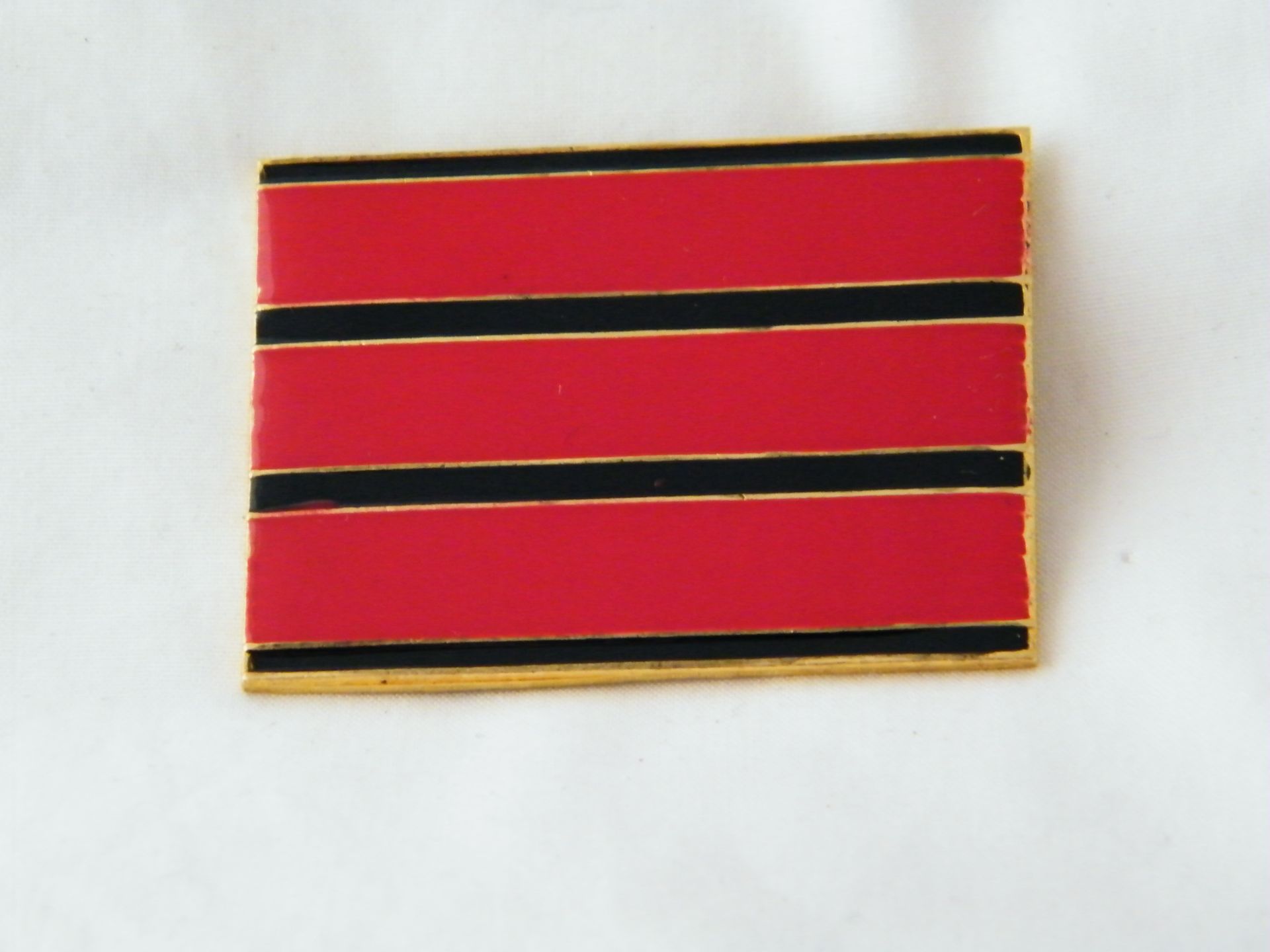 Un alfiler rojo y negro con rayas doradas sobre una superficie blanca.