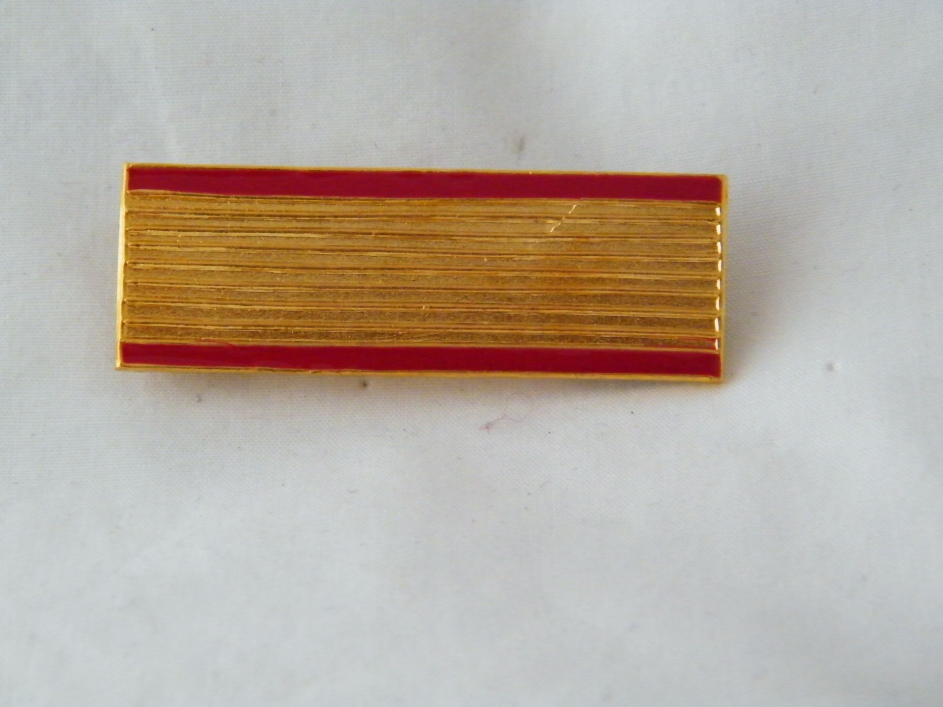 Un alfiler dorado con una raya roja.