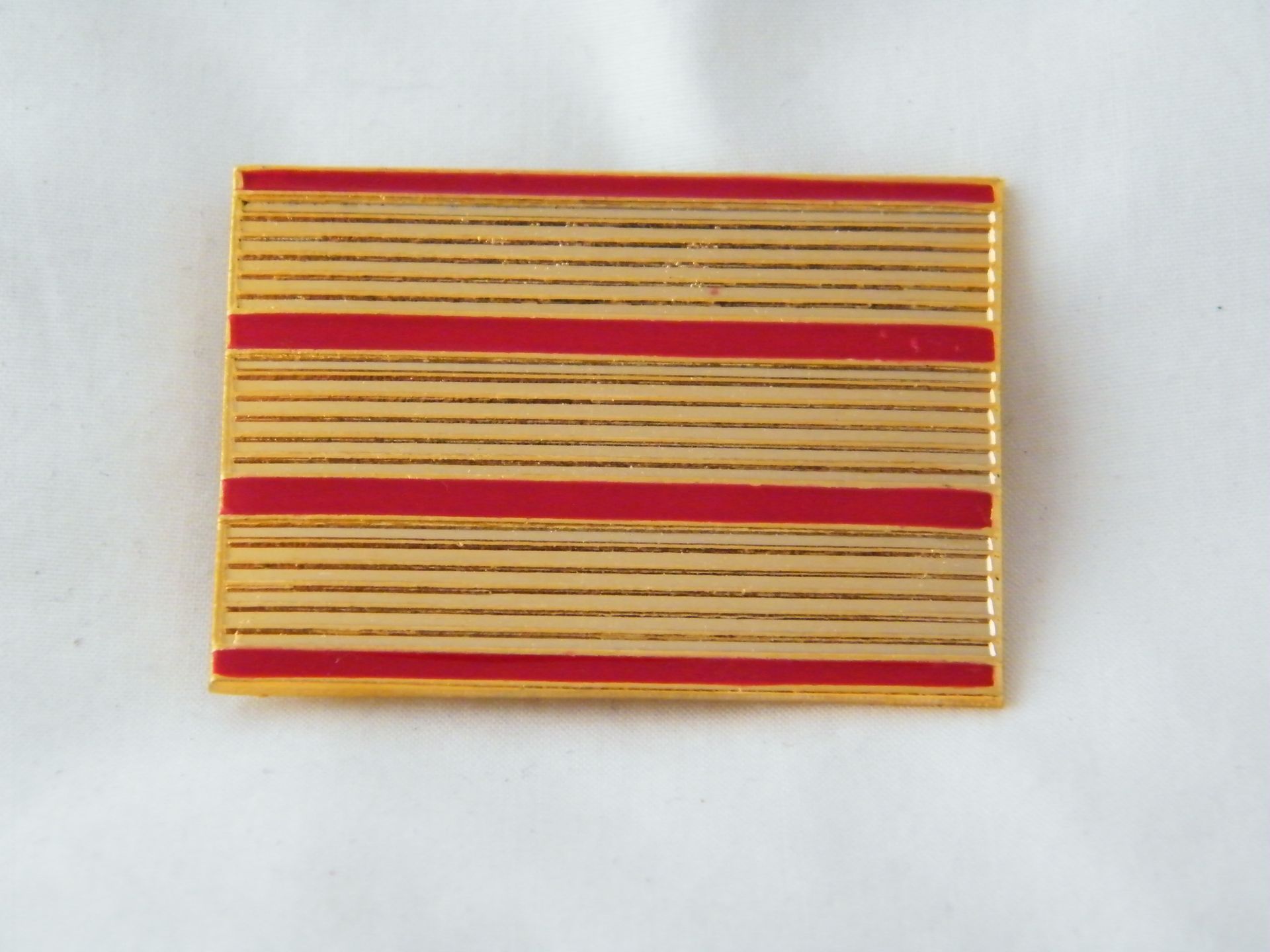 Un alfiler dorado con tres rayas rojas.