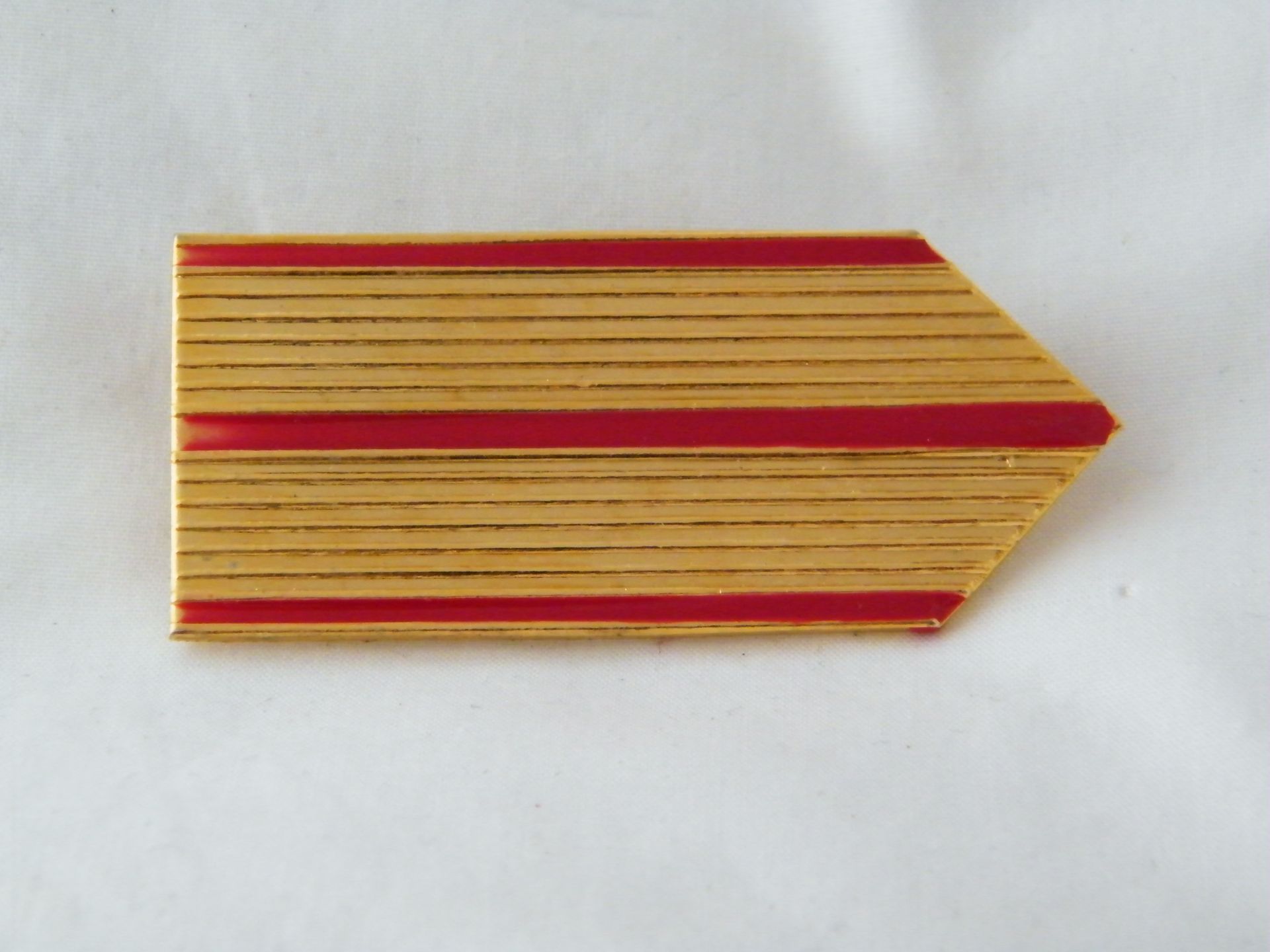 Una flecha dorada con rayas rojas sobre una superficie blanca