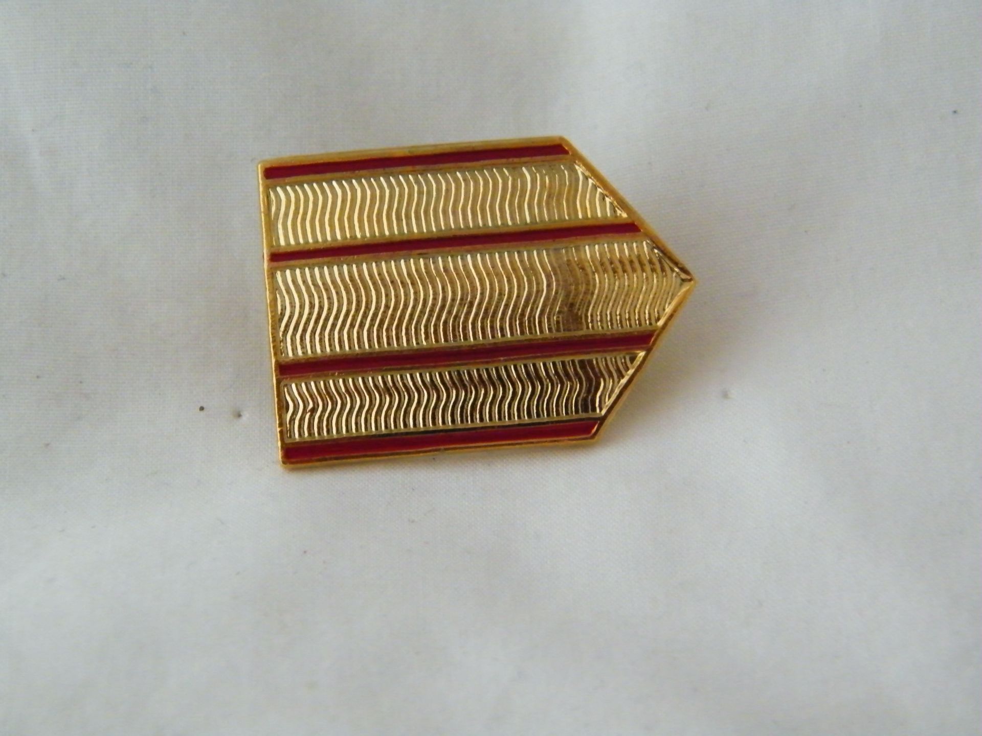 Un alfiler dorado con rayas rojas sobre una superficie blanca