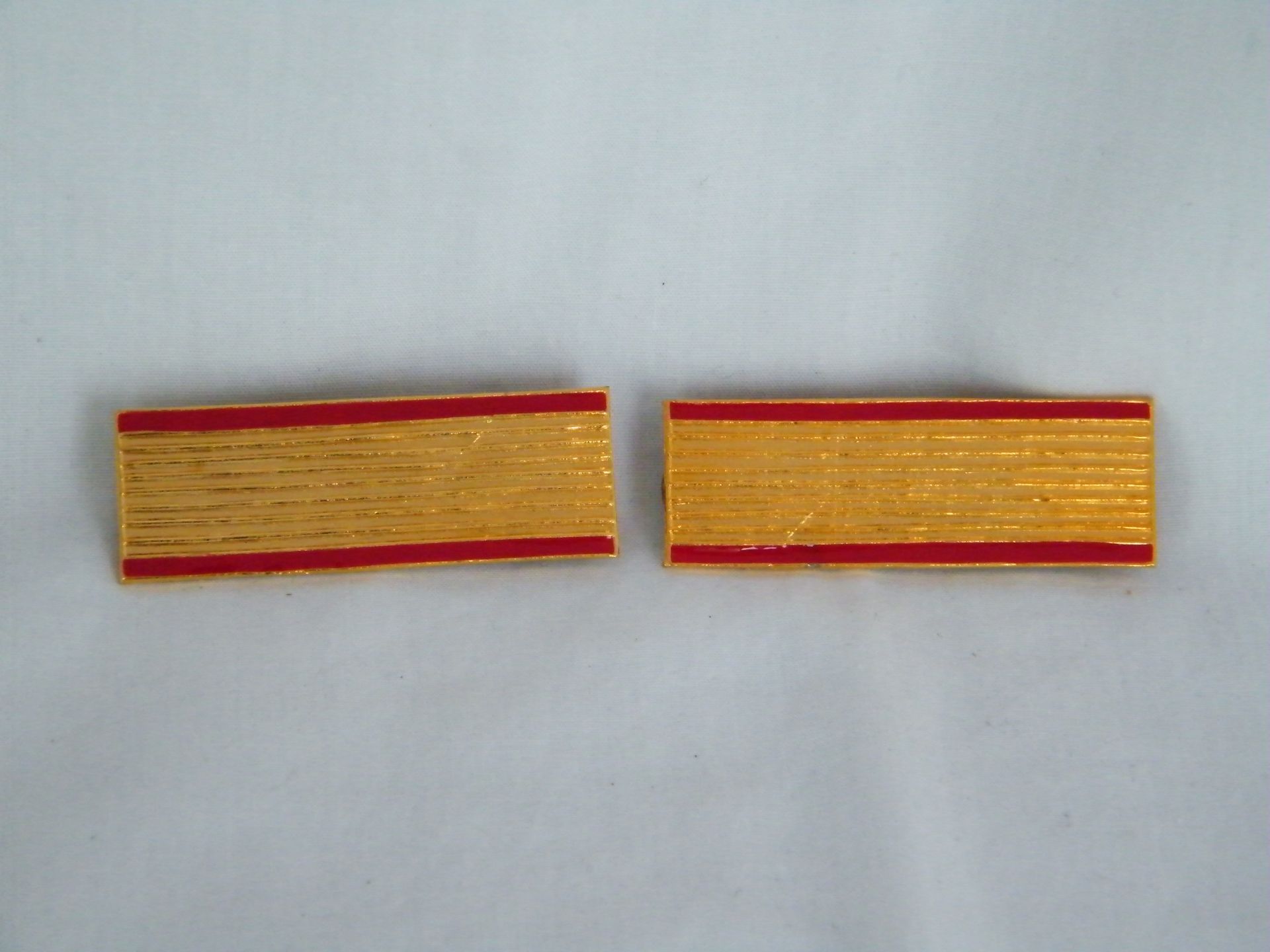 Un par de cintas doradas y rojas sobre una superficie blanca.