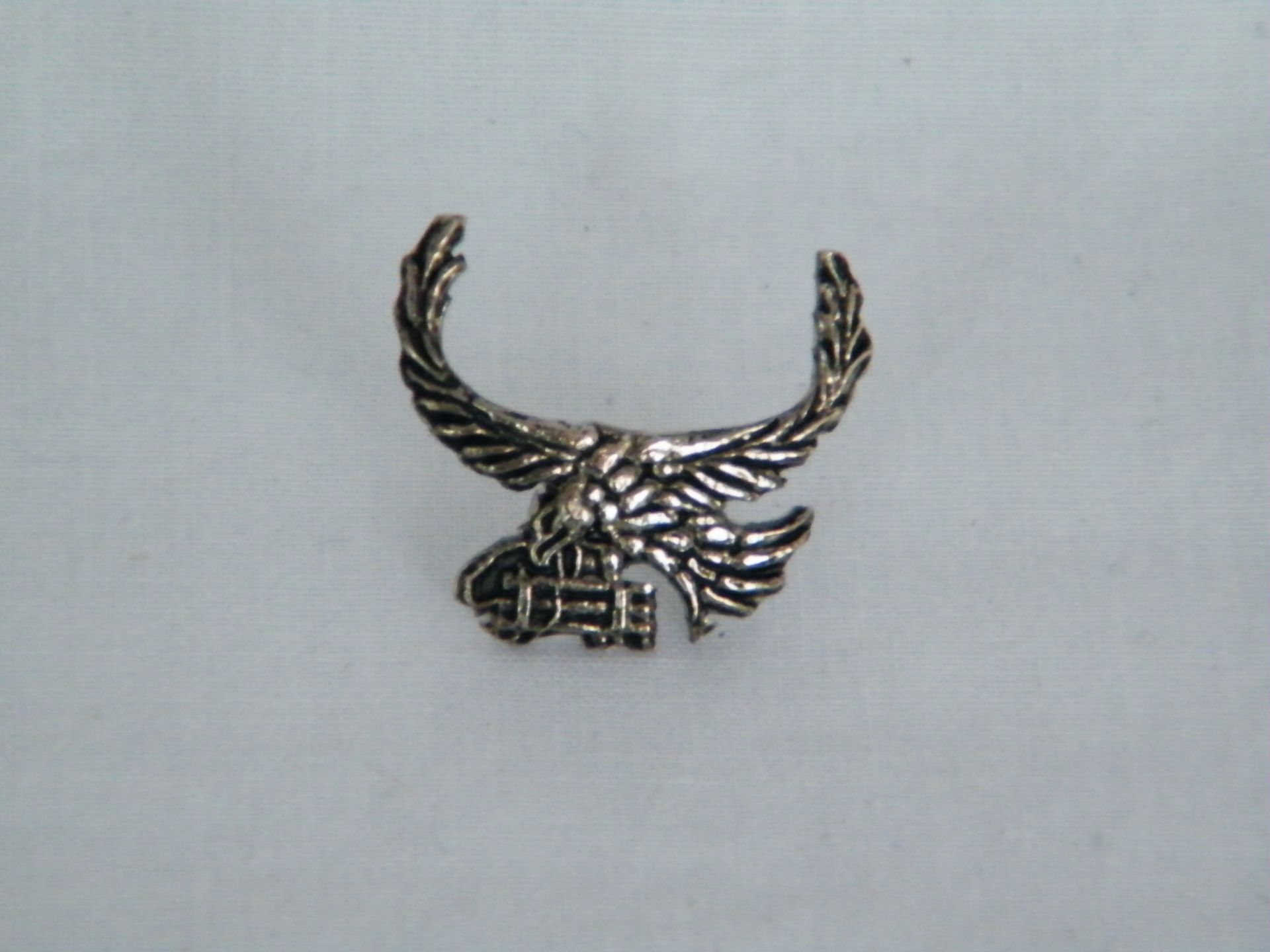 Un águila plateada con las alas extendidas está sentada sobre una superficie blanca.