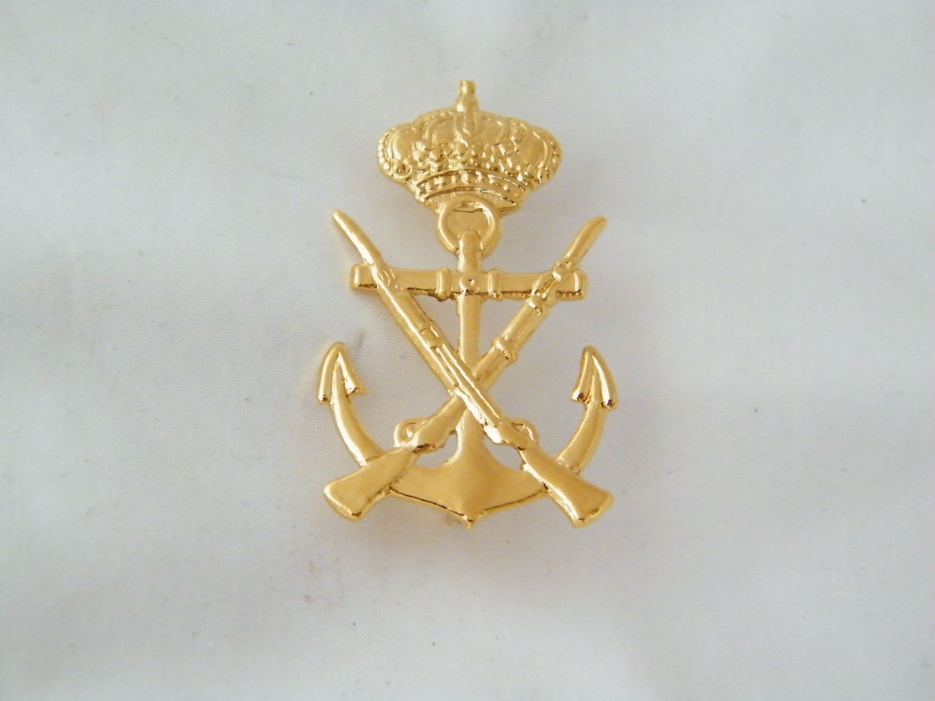 Un ancla de oro con dos espadas cruzadas y una corona en la parte superior.