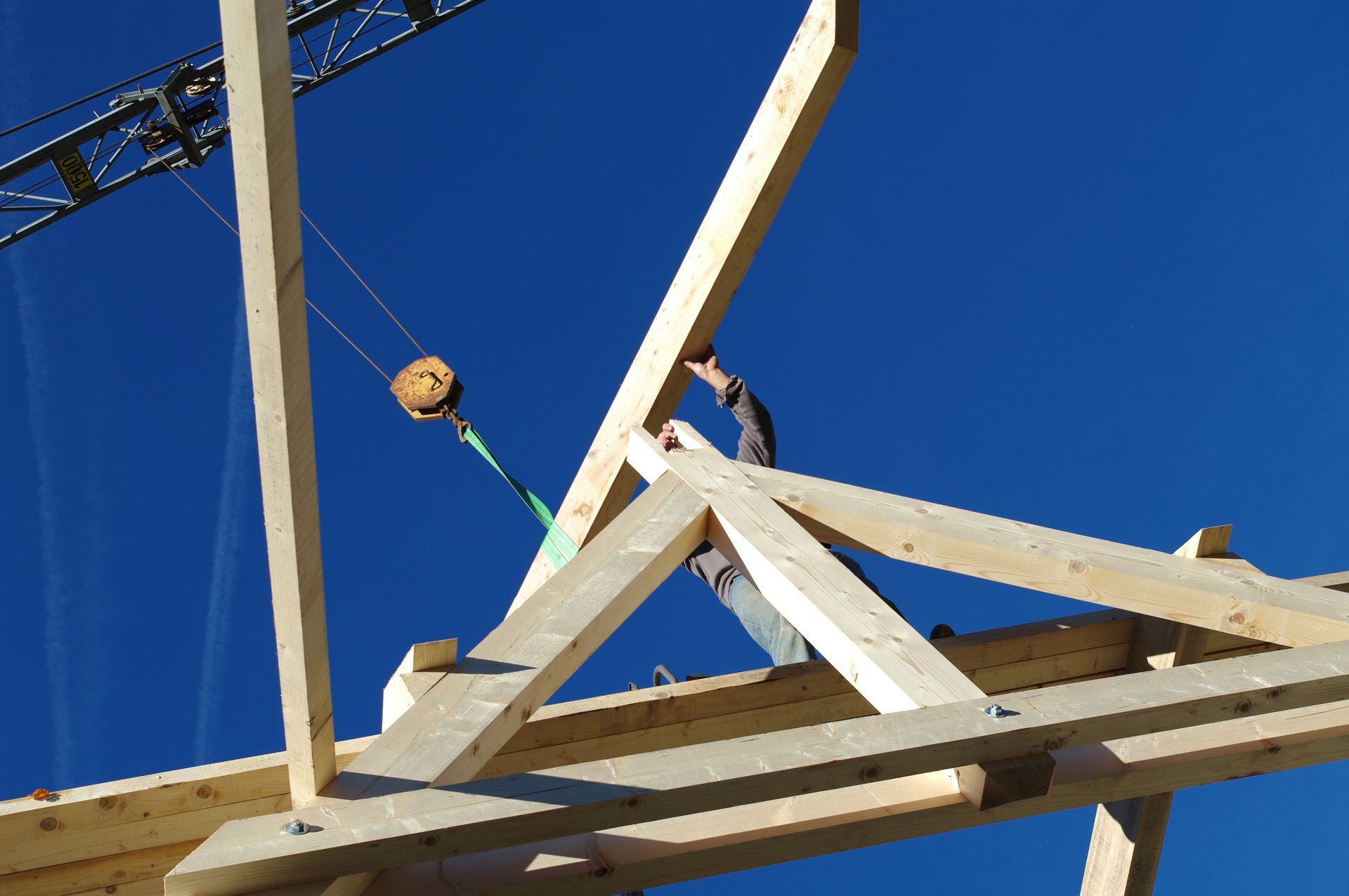Un ouvrier du bâtiment guide une poutre en bois descendue par une grue sur une charpente.