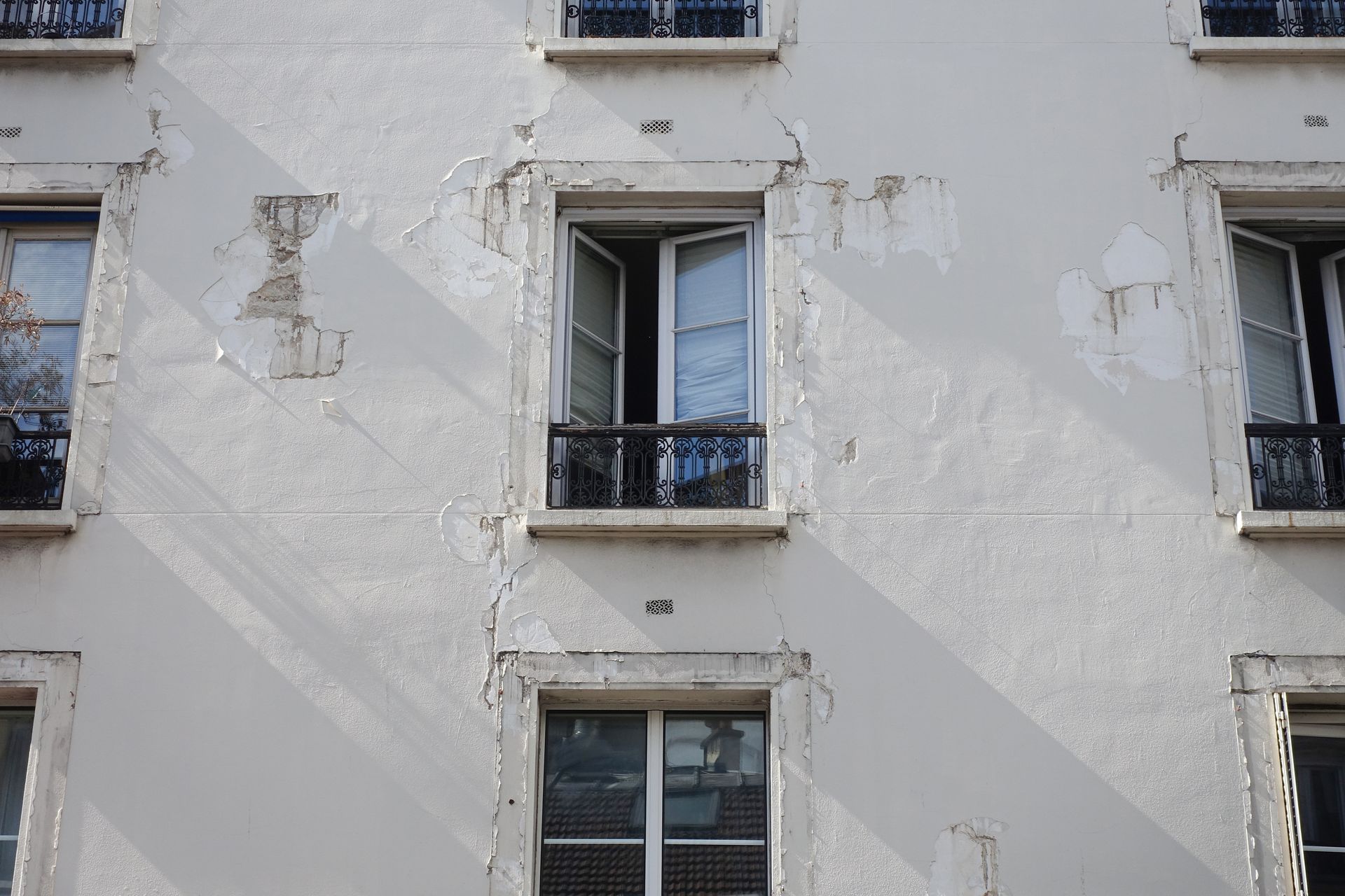 Une façade d'un bâtiment présentant d'importantes traces d'écaillage de la peinture et des fissures autour des cadres.