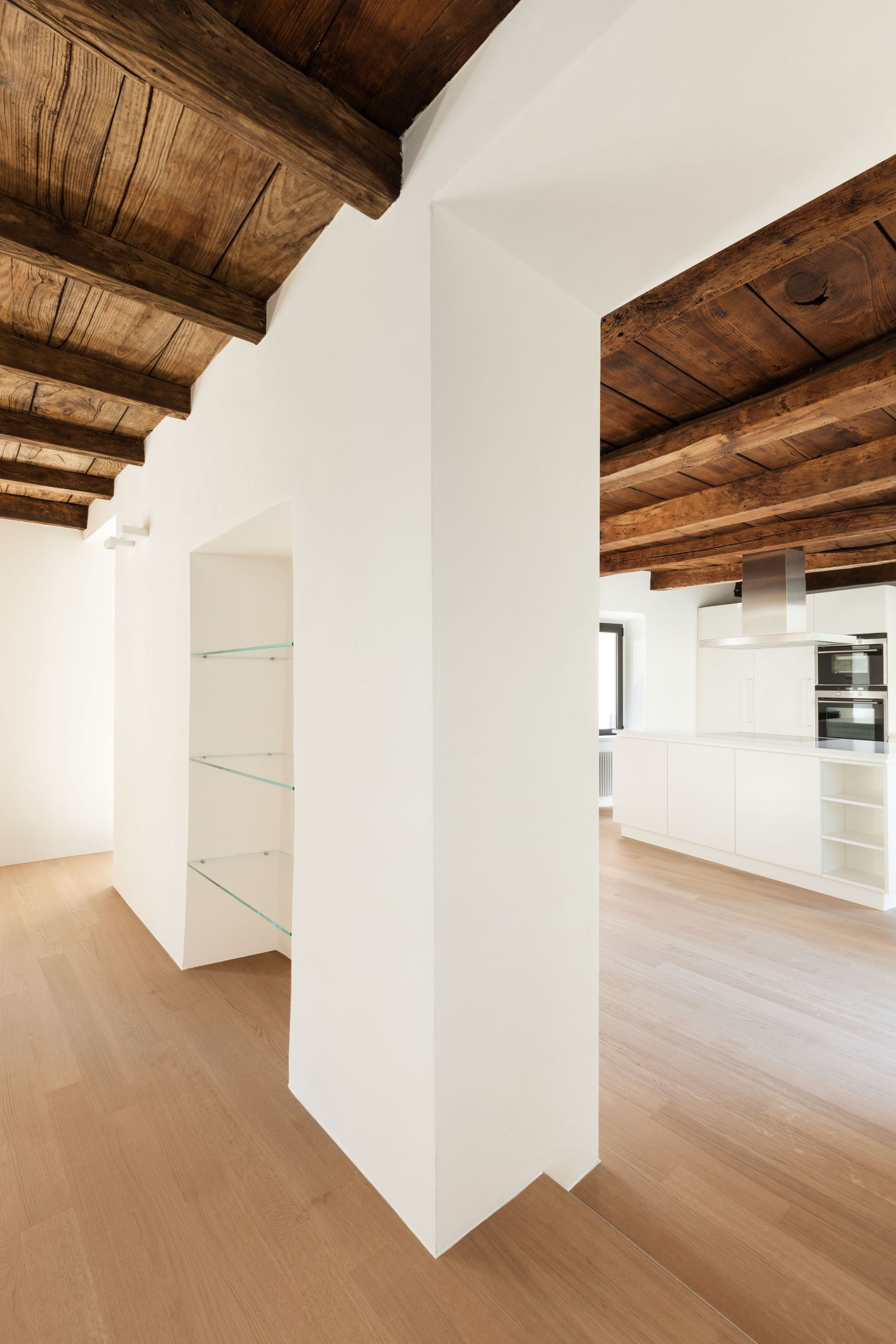 Un intérieur moderne avec des murs blancs, un parquet clair et des poutres apparentes au plafond.